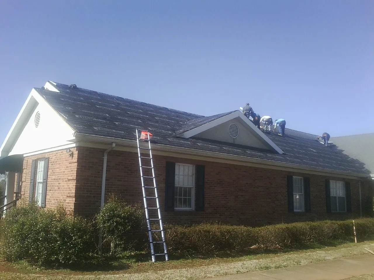 Crew tearing shingles off a brick ranch roof with a ladder set — Emergency Roof Repair work by our crew in Vincentown