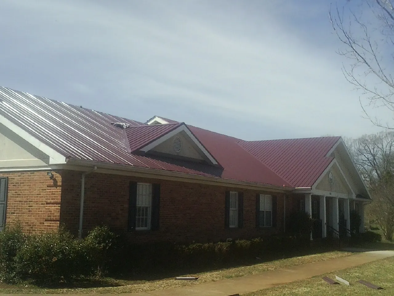 Red metal roof with gabled entries on a long brick building, from a Hail Damage Roof Repair job in Vincentown