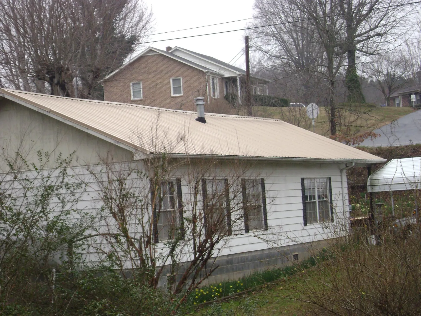 Tan metal roof on a white sided house set into a hillside — Commercial Roofing by Roofing Brothers in Vincentown